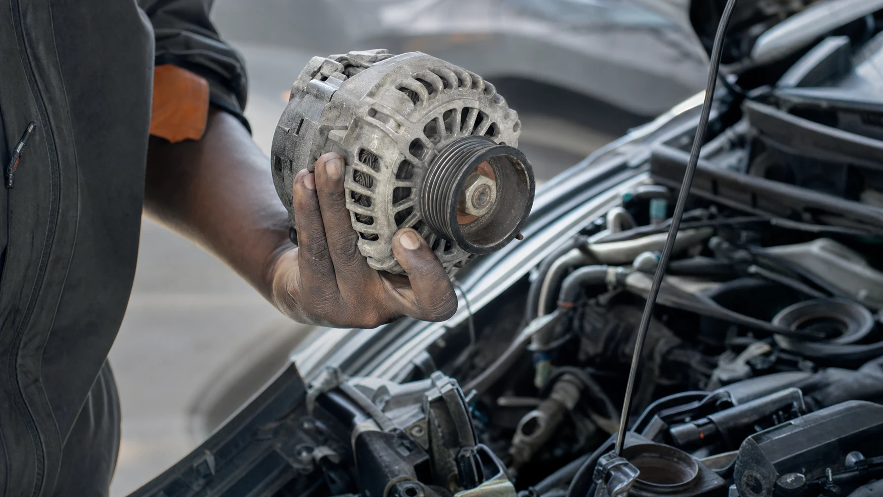 A mechanic holding a removed alternator next to a car's open engine bay