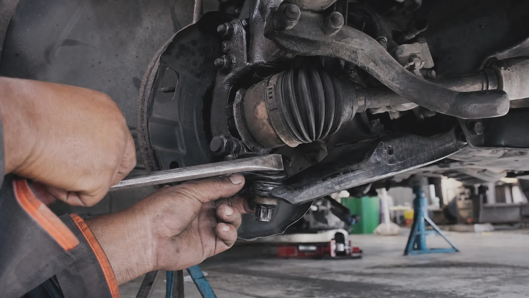 A mechanic using a pry bar to check a front suspension ball joint for play