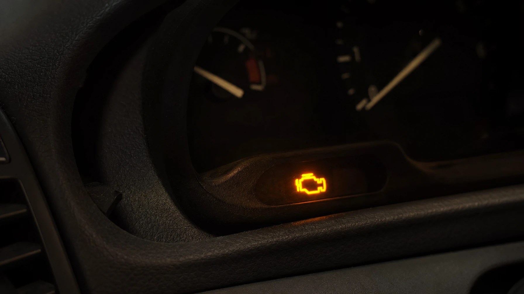 A glowing amber check engine warning icon lit up on a dark car dashboard instrument cluster