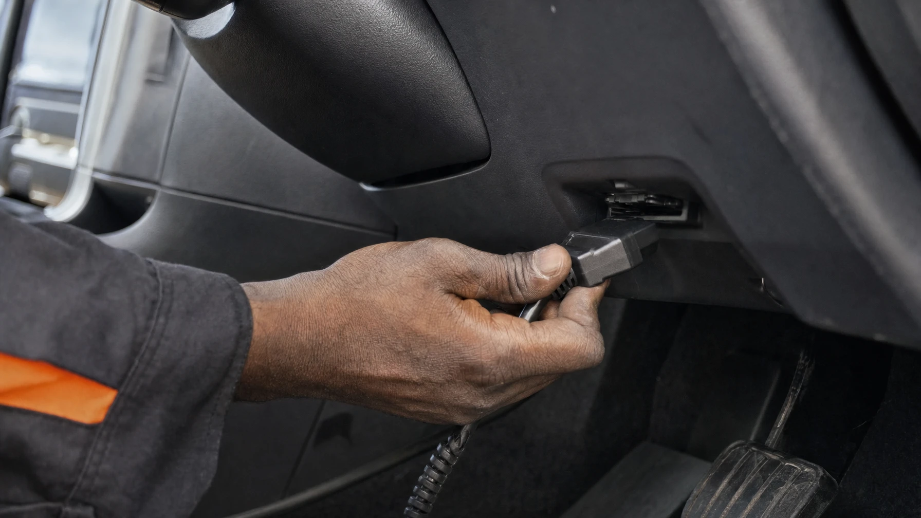 A mechanic plugging an OBD-II code scanner into a car's diagnostic port under the dashboard