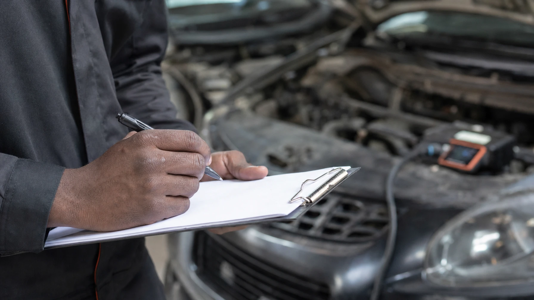A mechanic writing a quote on a clipboard next to a car with a diagnostic scanner plugged in