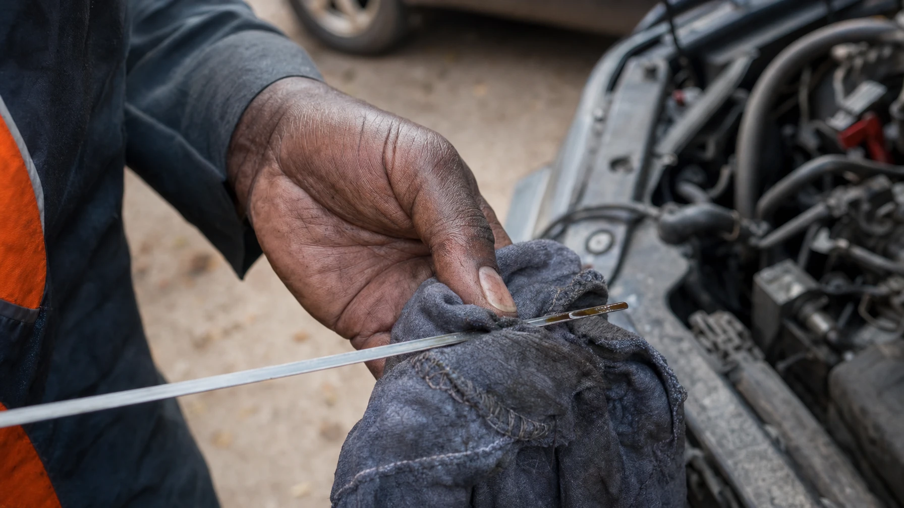 A hand wiping a transmission dipstick clean with a rag in a driveway before checking the fluid level