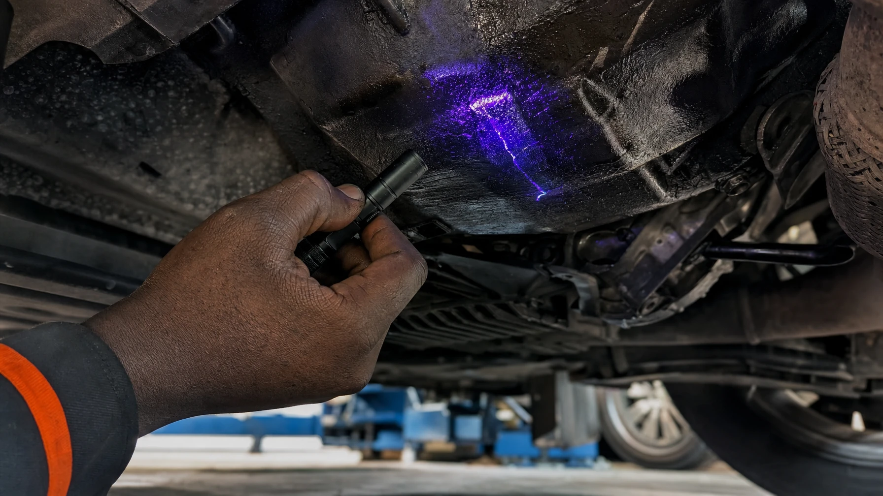 A mechanic using a UV flashlight underneath a car to trace an oil leak