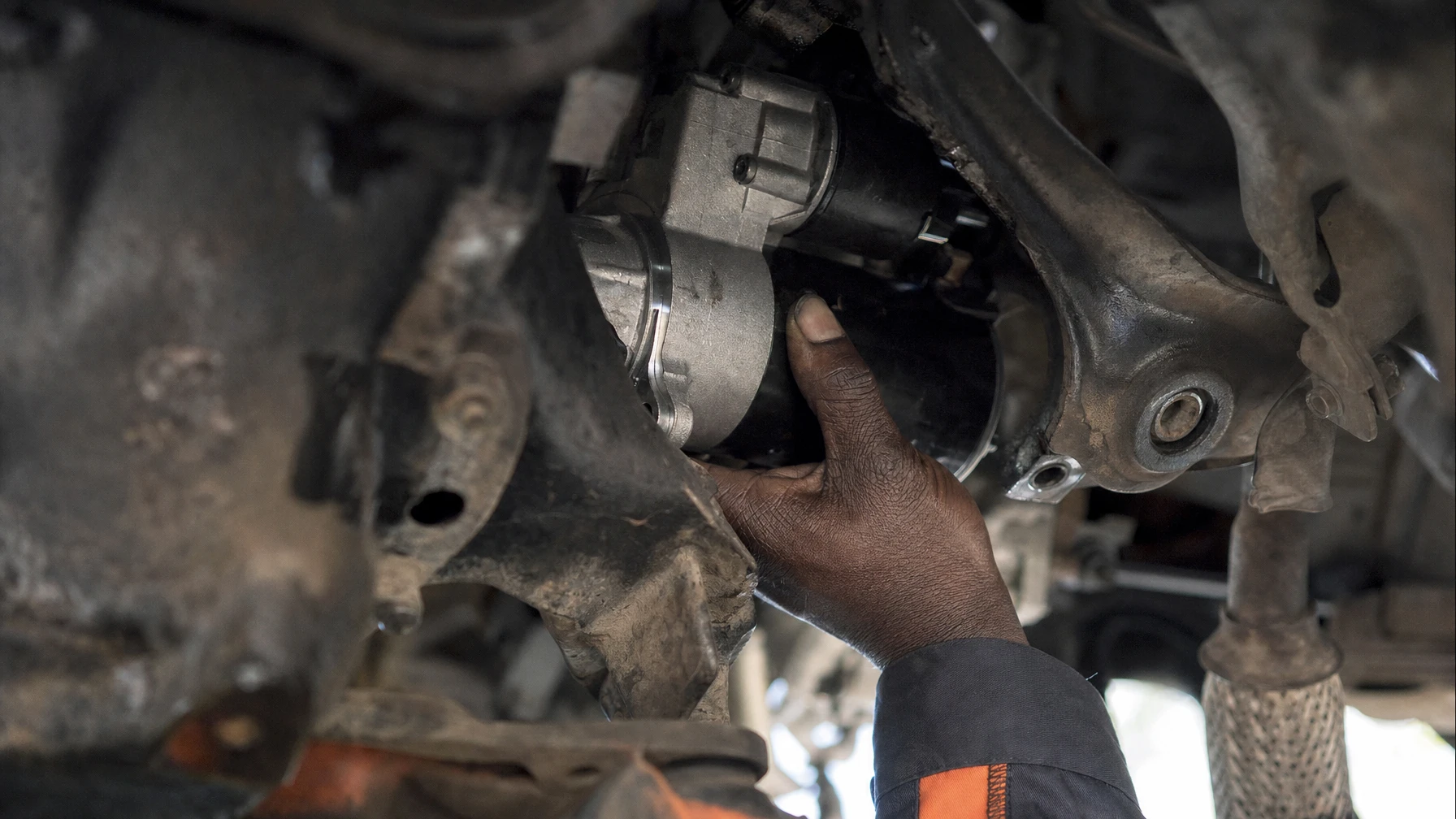 A mechanic's hand installing a car starter motor from underneath the vehicle